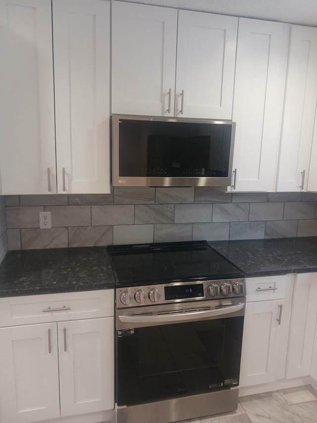 kitchen with white cabinets, backsplash, appliances with stainless steel finishes, and dark stone countertops