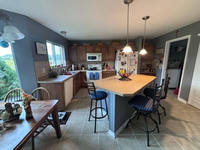 kitchen with white appliances, hanging light fixtures, tile patterned flooring, tasteful backsplash, and a breakfast bar area