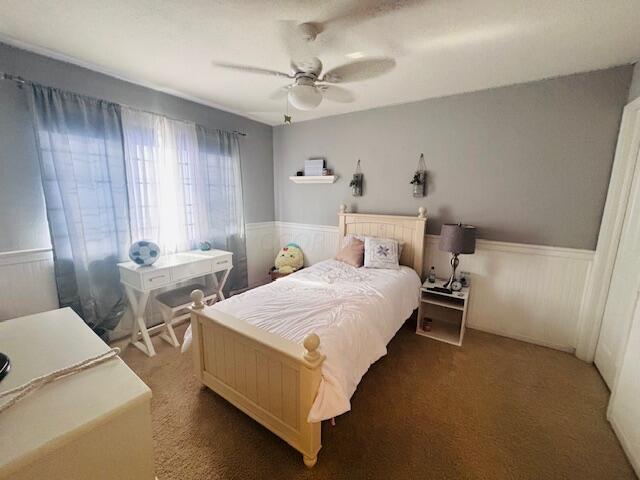 bedroom with dark colored carpet, ceiling fan, and wooden walls