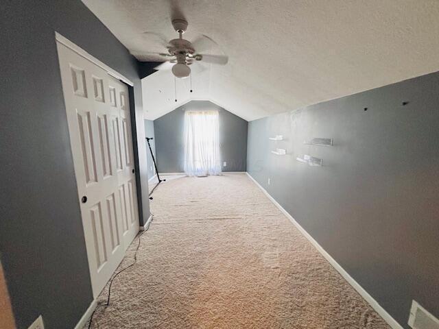 interior space with carpet, ceiling fan, a textured ceiling, and vaulted ceiling