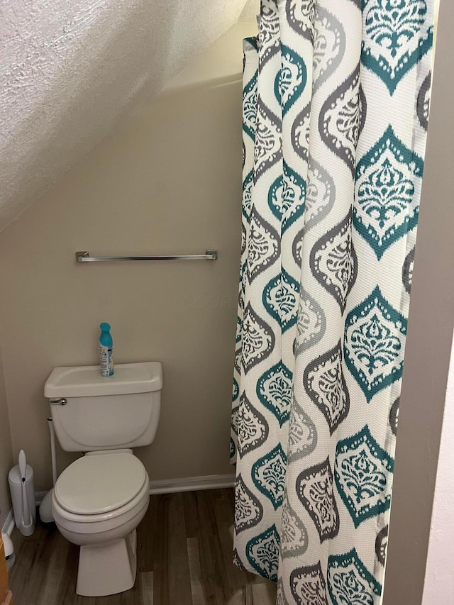 bathroom featuring vaulted ceiling, a textured ceiling, a shower with curtain, toilet, and wood finished floors
