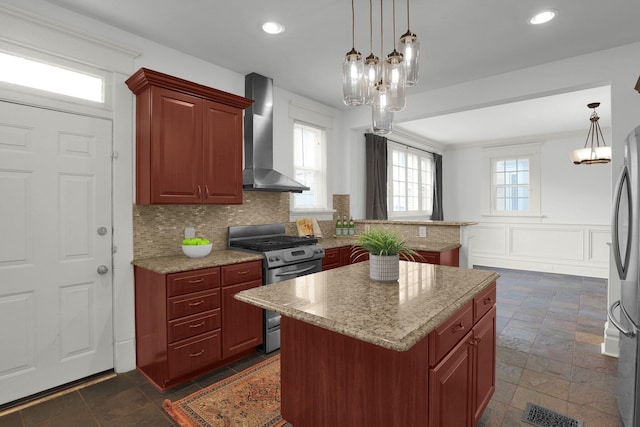 kitchen with gas range, a center island, wall chimney exhaust hood, hanging light fixtures, and backsplash