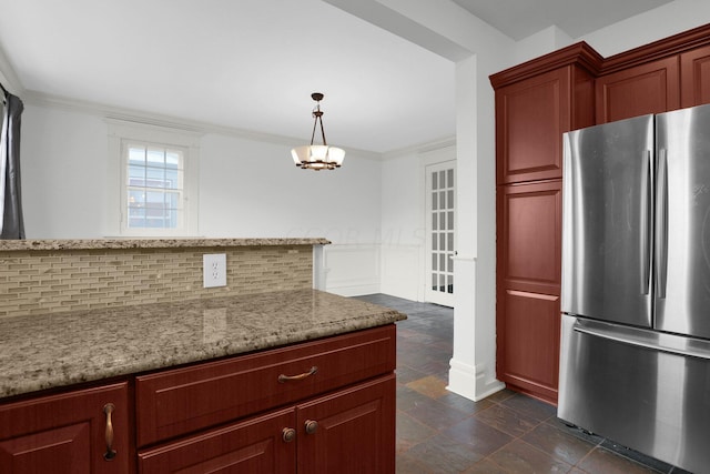 kitchen featuring stainless steel refrigerator, hanging light fixtures, light stone counters, decorative backsplash, and ornamental molding