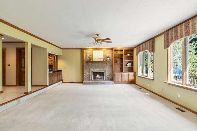 unfurnished living room featuring ceiling fan, ornamental molding, light colored carpet, and a brick fireplace