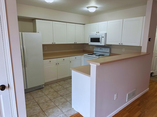 kitchen with white cabinets, kitchen peninsula, a textured ceiling, white appliances, and light tile patterned floors