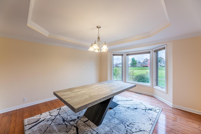 dining area with a raised ceiling, light wood-type flooring, crown molding, and an inviting chandelier