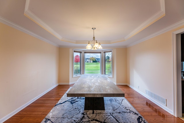 dining space featuring wood-type flooring, a raised ceiling, crown molding, and a notable chandelier