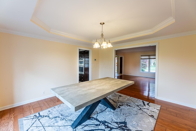 dining area with a tray ceiling, an inviting chandelier, dark wood-type flooring, and ornamental molding