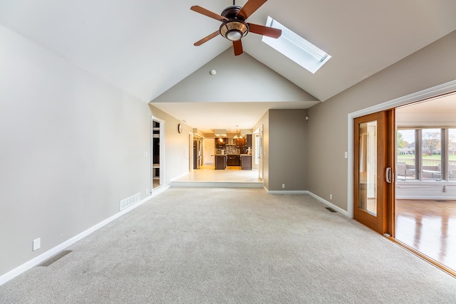 unfurnished living room featuring light carpet, a skylight, high vaulted ceiling, and ceiling fan