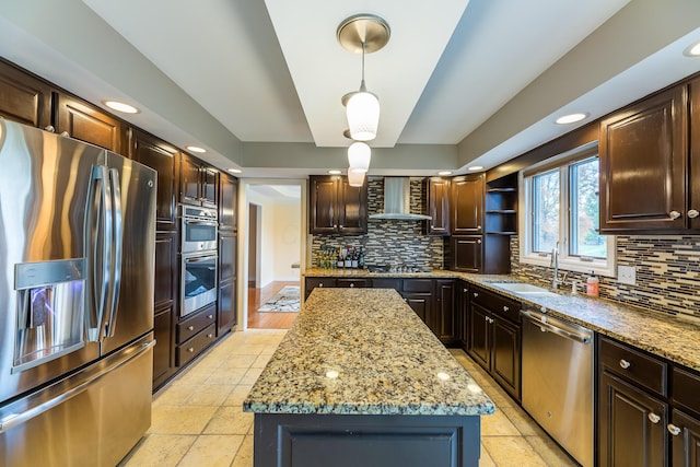 kitchen with wall chimney range hood, hanging light fixtures, decorative backsplash, appliances with stainless steel finishes, and a kitchen island