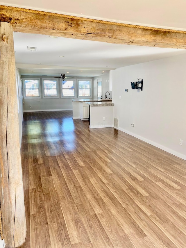 unfurnished living room featuring wood-type flooring, beam ceiling, and sink