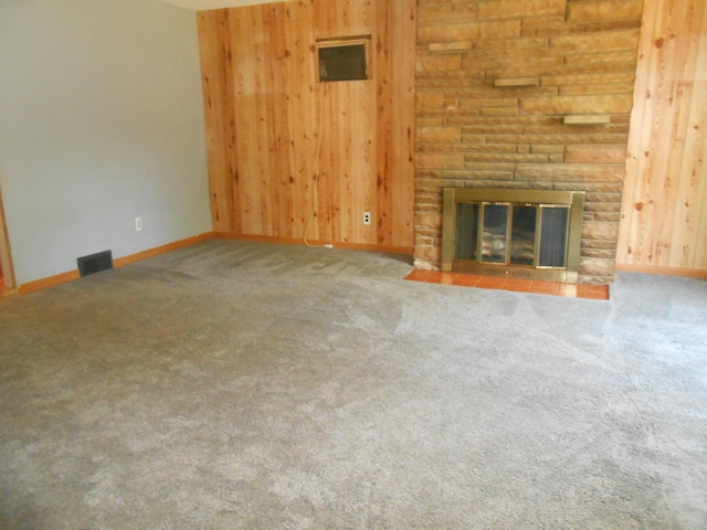 unfurnished living room with carpet flooring, a stone fireplace, and wood walls