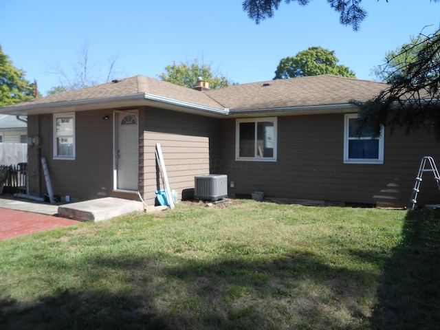 rear view of house with central air condition unit and a lawn