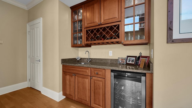 bar with sink, beverage cooler, dark stone countertops, crown molding, and hardwood / wood-style floors