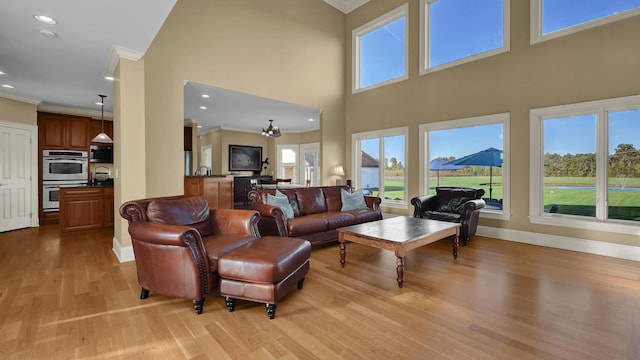 living room with an inviting chandelier, a towering ceiling, crown molding, and light hardwood / wood-style flooring