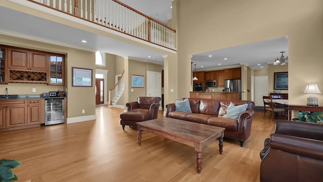 living room with light hardwood / wood-style flooring, a towering ceiling, beverage cooler, and indoor wet bar