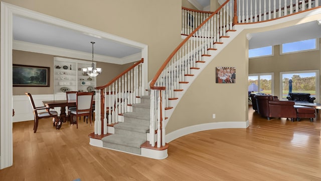 stairway with a high ceiling, hardwood / wood-style flooring, built in features, ornamental molding, and a notable chandelier