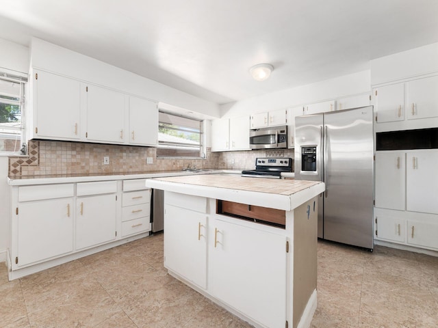 kitchen with white cabinets, appliances with stainless steel finishes, a center island, and tasteful backsplash