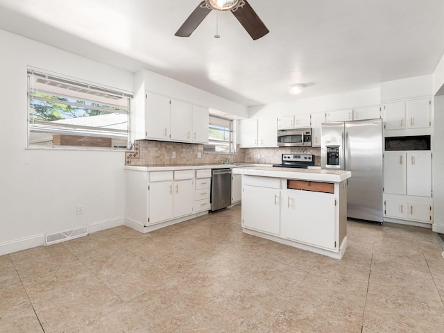 kitchen with appliances with stainless steel finishes, tasteful backsplash, a kitchen island, ceiling fan, and white cabinetry