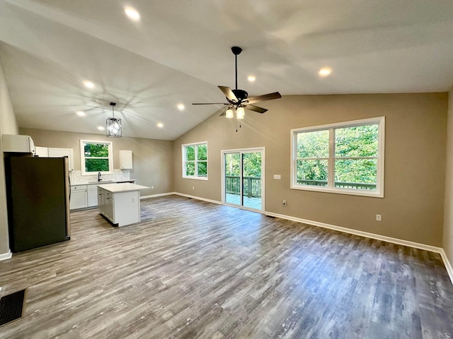 unfurnished living room featuring ceiling fan with notable chandelier, light wood-type flooring, sink, and vaulted ceiling