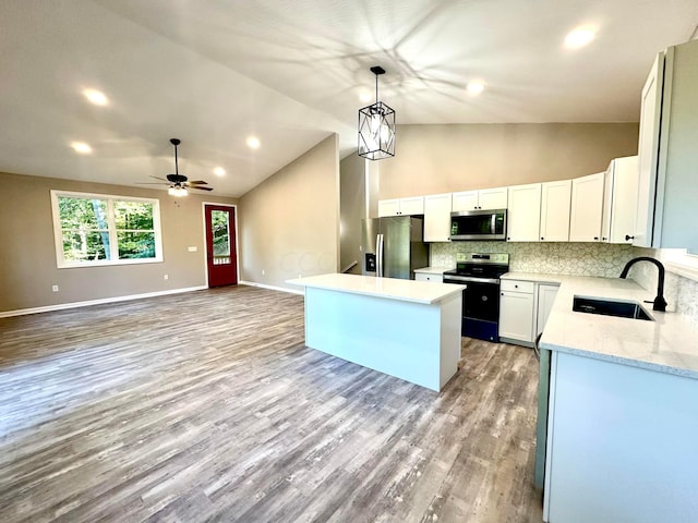 kitchen featuring stainless steel appliances, vaulted ceiling, sink, white cabinets, and a center island