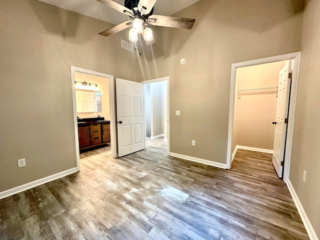 unfurnished bedroom featuring a towering ceiling, a walk in closet, ceiling fan, hardwood / wood-style floors, and a closet