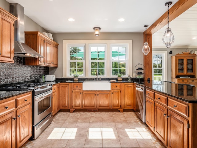 kitchen featuring hanging light fixtures, sink, wall chimney exhaust hood, dark stone countertops, and appliances with stainless steel finishes