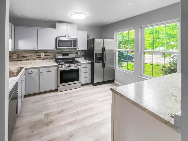 kitchen with white cabinets, sink, decorative backsplash, appliances with stainless steel finishes, and light hardwood / wood-style floors