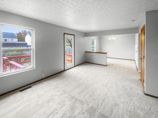 unfurnished room featuring light colored carpet, a textured ceiling, and a chandelier