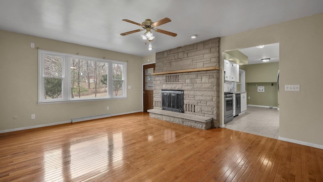 unfurnished living room featuring sink, light hardwood / wood-style flooring, ceiling fan, a baseboard heating unit, and a stone fireplace