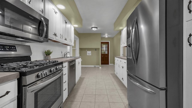 kitchen featuring light tile patterned flooring, sink, appliances with stainless steel finishes, white cabinets, and backsplash