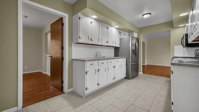 kitchen featuring appliances with stainless steel finishes, light tile patterned floors, white cabinets, and backsplash