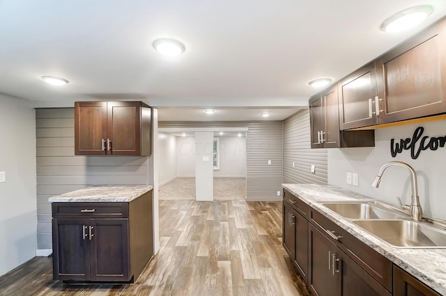 kitchen with sink, light hardwood / wood-style flooring, dark brown cabinets, and light stone countertops