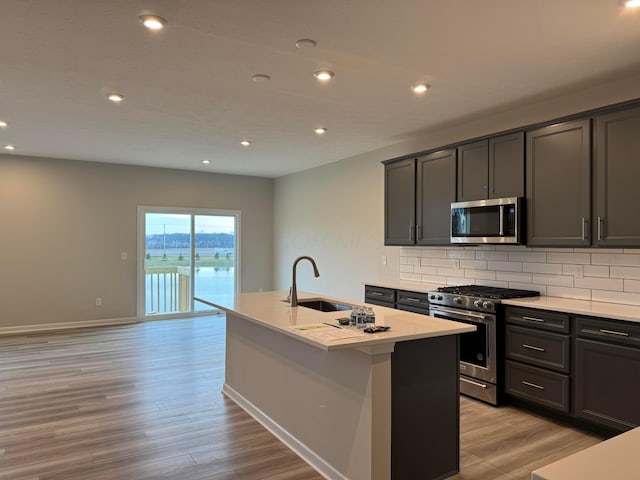 kitchen with decorative backsplash, stainless steel appliances, sink, a center island with sink, and light hardwood / wood-style flooring