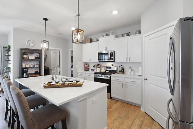 kitchen featuring pendant lighting, stainless steel appliances, white cabinetry, and a kitchen island with sink