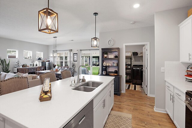 kitchen featuring light wood-type flooring, sink, pendant lighting, white cabinetry, and an island with sink