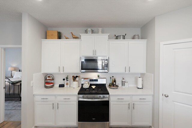 kitchen with backsplash, a textured ceiling, stainless steel appliances, white cabinets, and light hardwood / wood-style floors