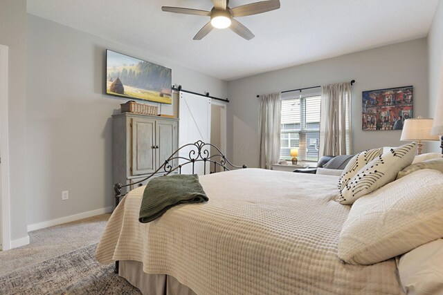 carpeted bedroom with ceiling fan and a barn door