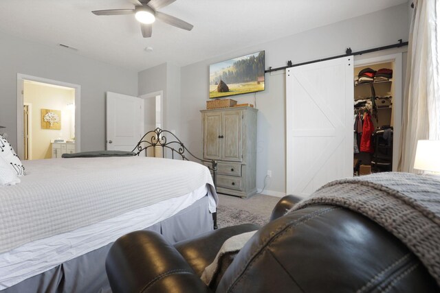 bedroom featuring ensuite bath, ceiling fan, a barn door, a walk in closet, and a closet