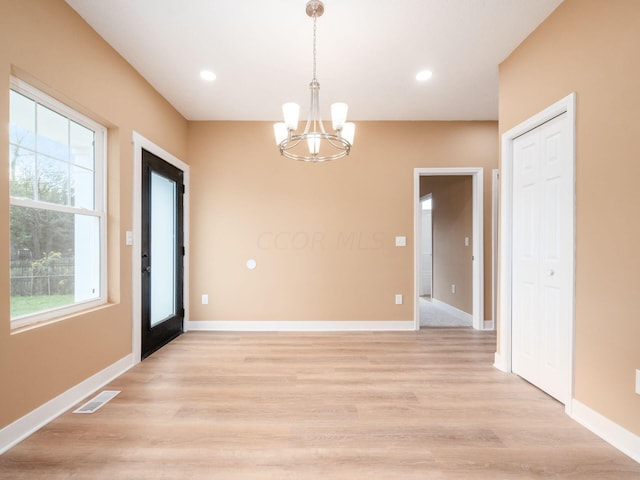 unfurnished dining area with plenty of natural light, light hardwood / wood-style floors, and an inviting chandelier