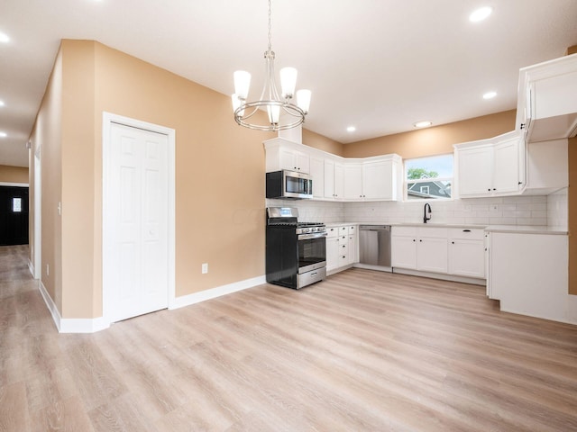 kitchen featuring white cabinetry, hanging light fixtures, stainless steel appliances, tasteful backsplash, and light wood-type flooring