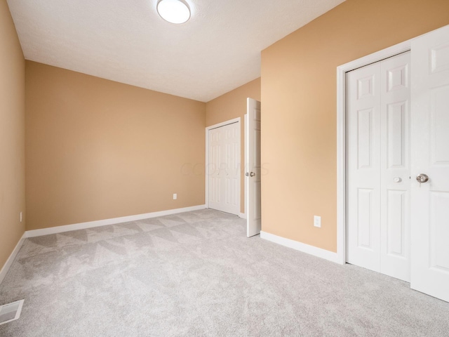 unfurnished bedroom featuring light colored carpet and two closets