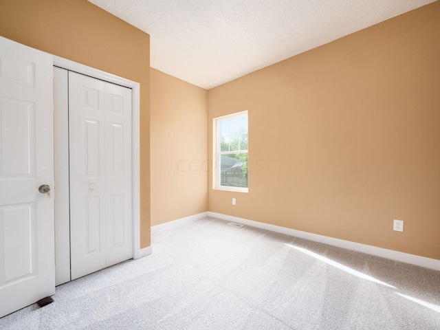 unfurnished bedroom with a textured ceiling, light colored carpet, and a closet