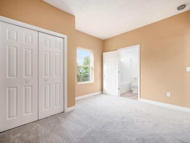 unfurnished bedroom featuring a closet, light colored carpet, and ensuite bath