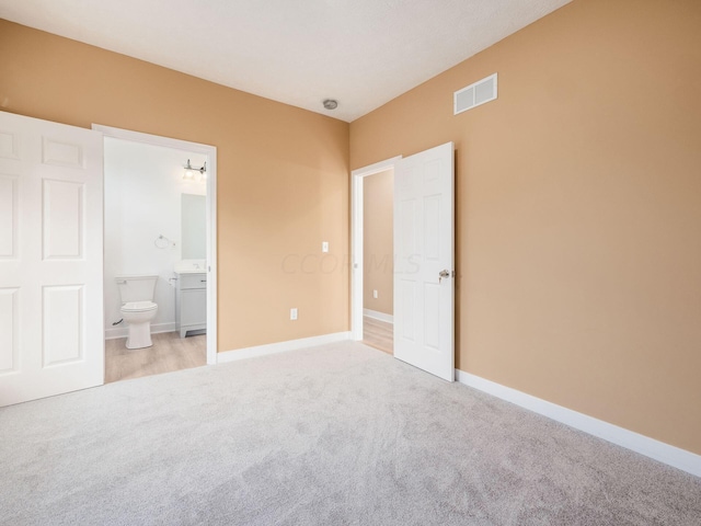 unfurnished bedroom with ensuite bathroom and light colored carpet