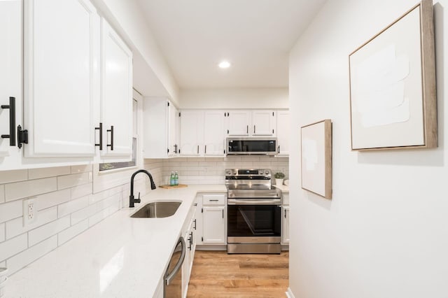 kitchen featuring sink, decorative backsplash, light hardwood / wood-style floors, white cabinetry, and stainless steel appliances