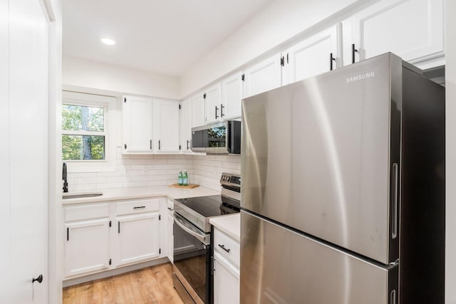 kitchen with backsplash, sink, light hardwood / wood-style flooring, white cabinetry, and stainless steel appliances