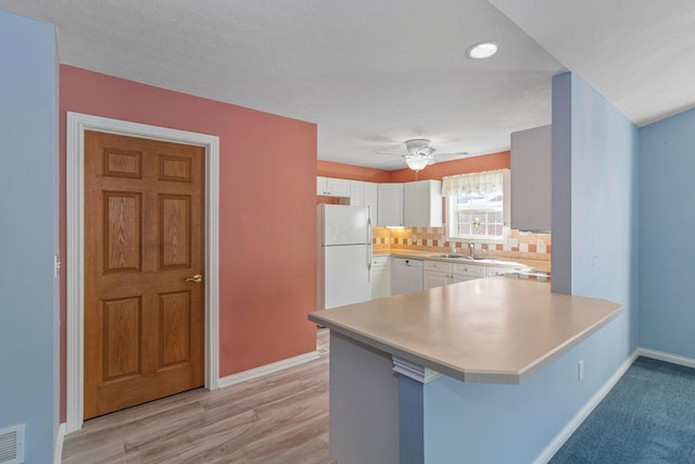 kitchen with kitchen peninsula, a kitchen bar, white appliances, light hardwood / wood-style flooring, and white cabinetry