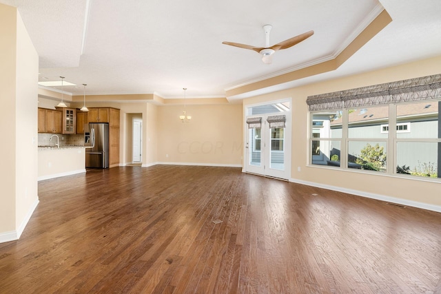 unfurnished living room with dark hardwood / wood-style flooring, a tray ceiling, ceiling fan, and ornamental molding