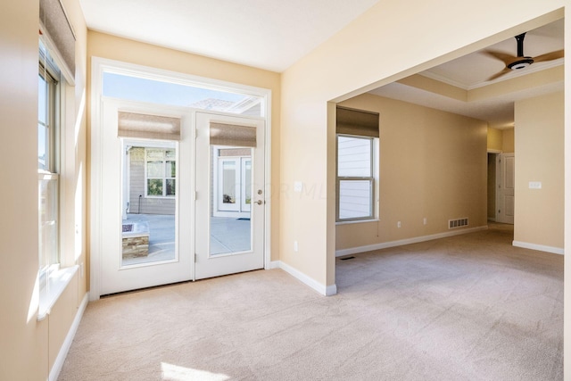 interior space with a raised ceiling, ceiling fan, crown molding, and light carpet